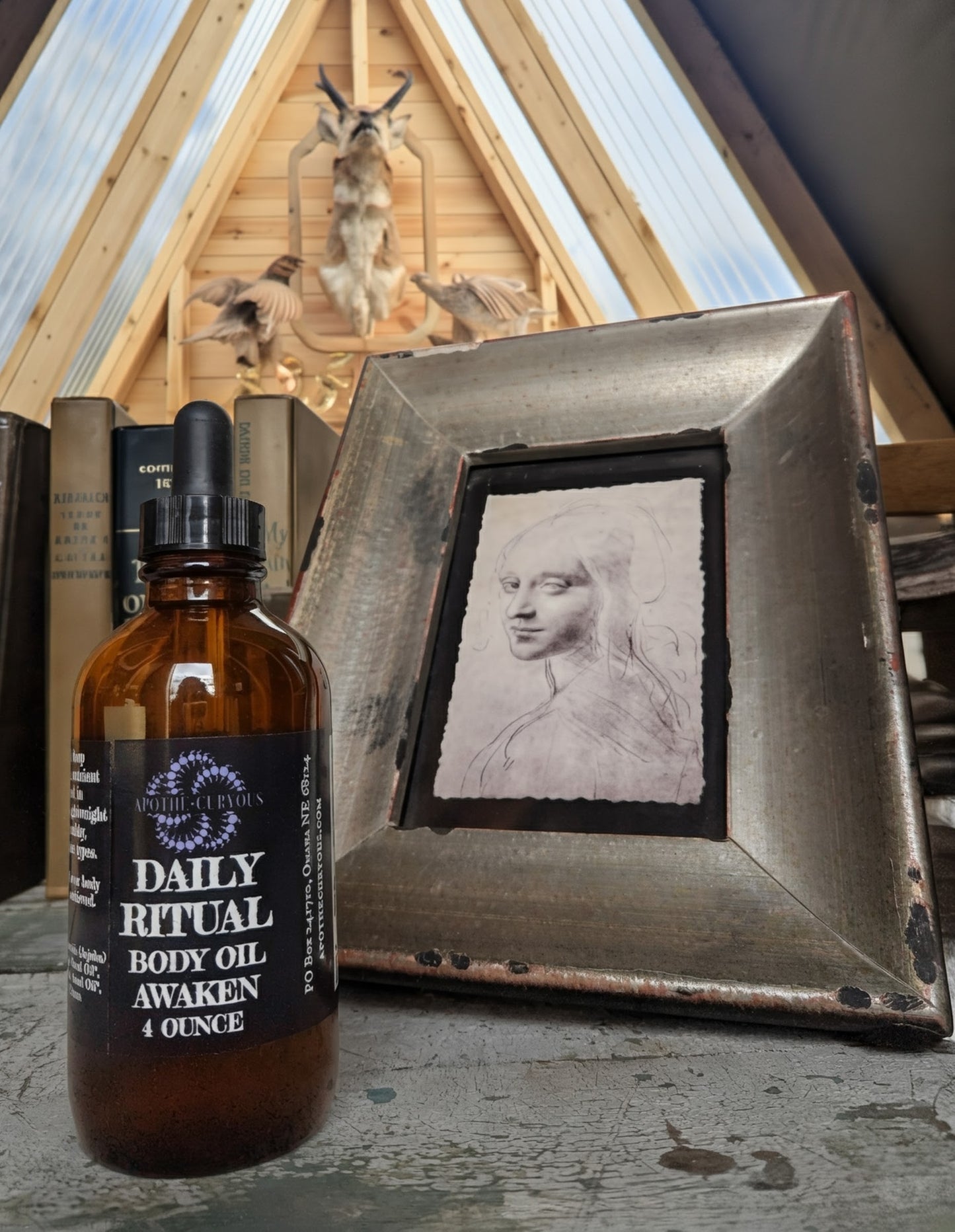Bottle of 'Daily Ritual Body Oil' with a rustic background featuring a framed portrait and wooden architecture.