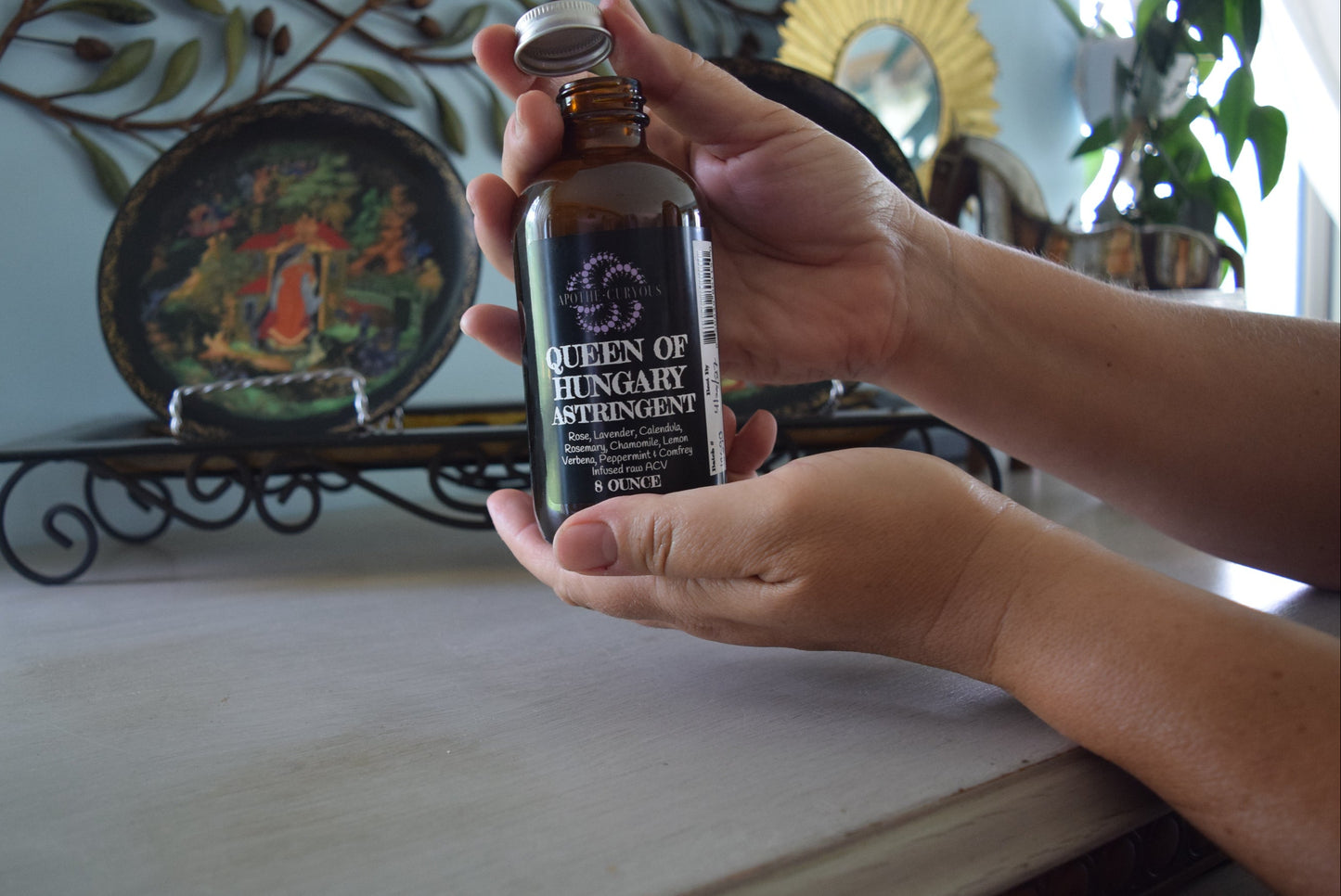Hands holding amber glass bottle of astringent, lid off, Apothecuryous
