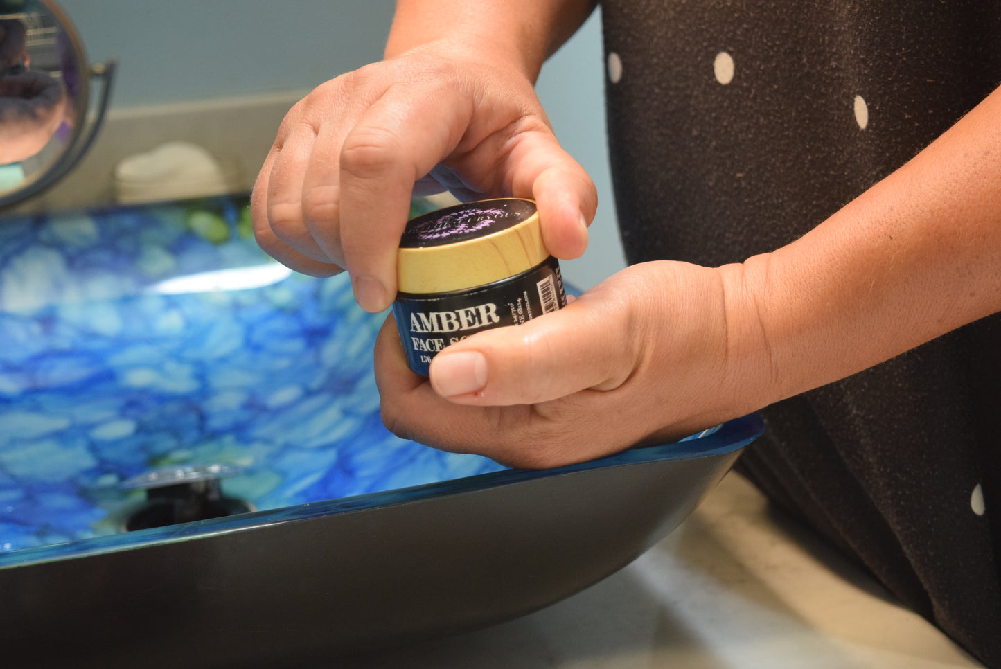 Hands opening jar of Amber Face scrub at bathroom sink, Apothecuryous