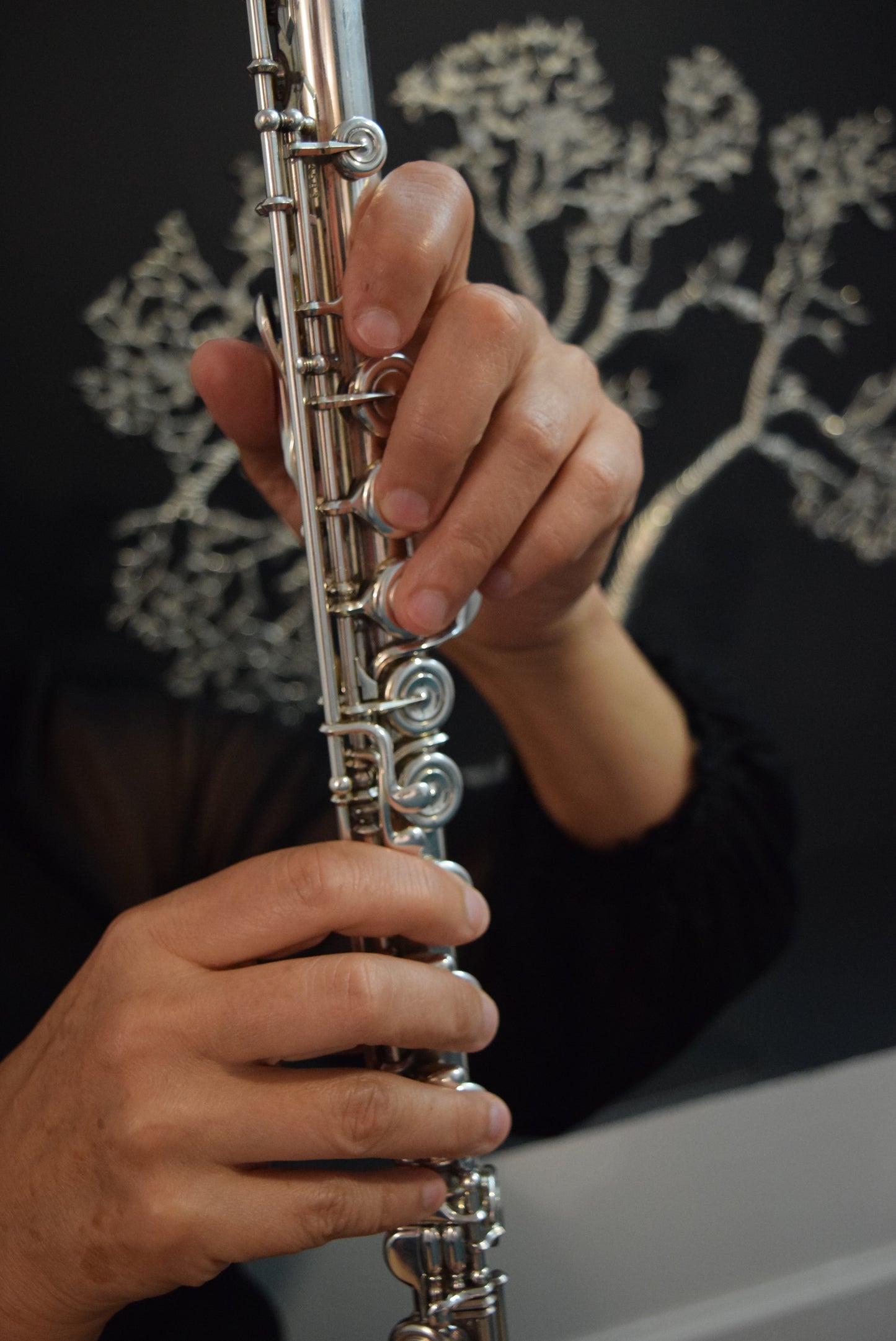 Hands holding flute upright, tree of life in background, Apothecuryous