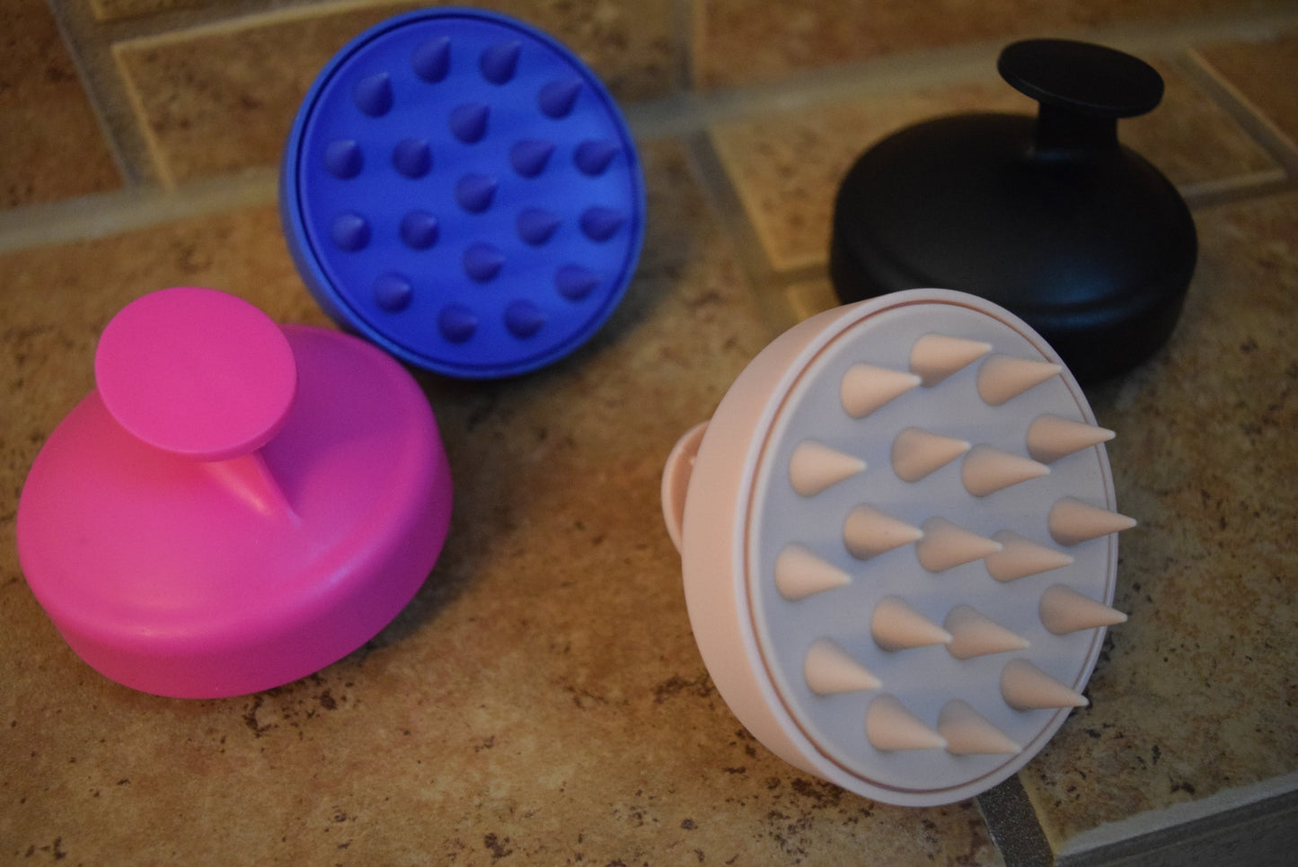 Four silicone scrubbers in different colors on a tiled surface