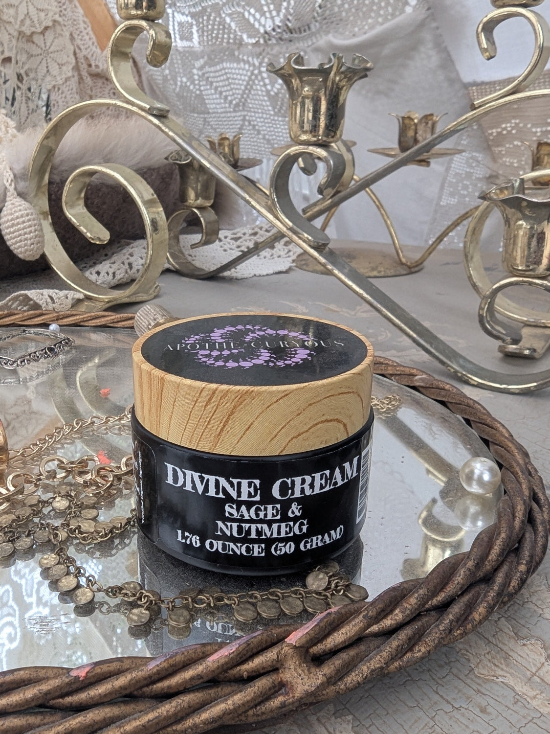 Divine cream in black glass jar on table with jewelry and mirror in background, Apothecuryous