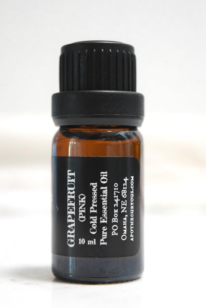 A small amber glass bottle of grapefruit cold pressed pure essential oil with a black cap and black label, photographed against a plain white background.
