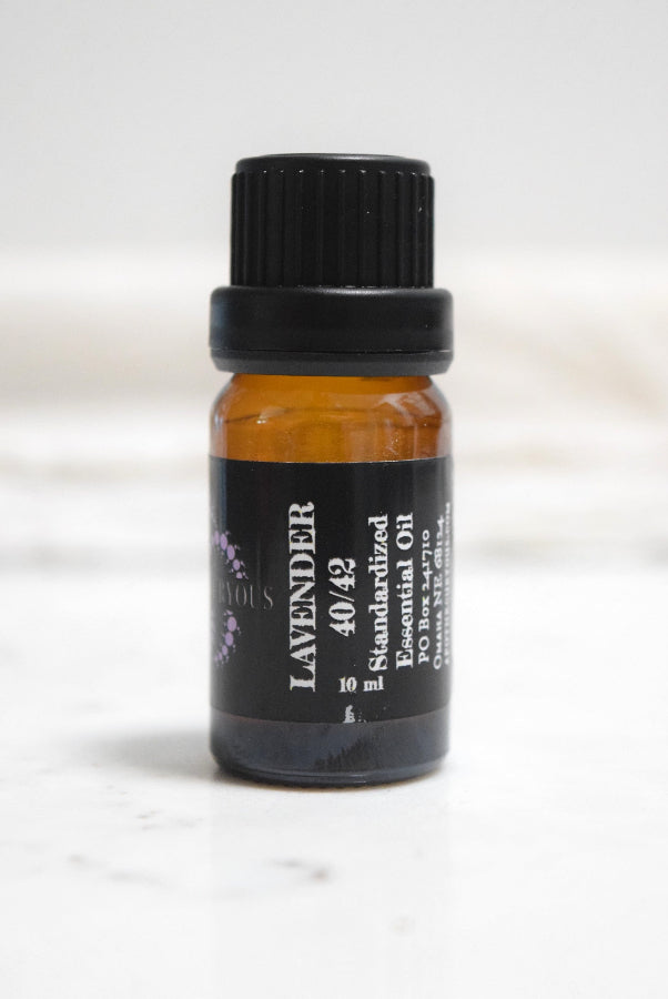 A small amber glass bottle of lavender essential oil with a black ribbed cap and a black label reading 'LAVENDER 40/42 Standardized Essential Oil' on a light marble-like surface.
