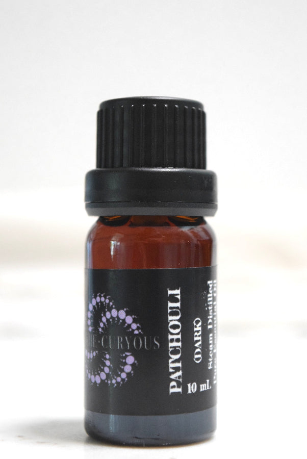 A 10 mL amber glass bottle of Patchouli essential oil with a black ribbed cap and a black label featuring purple and white text.