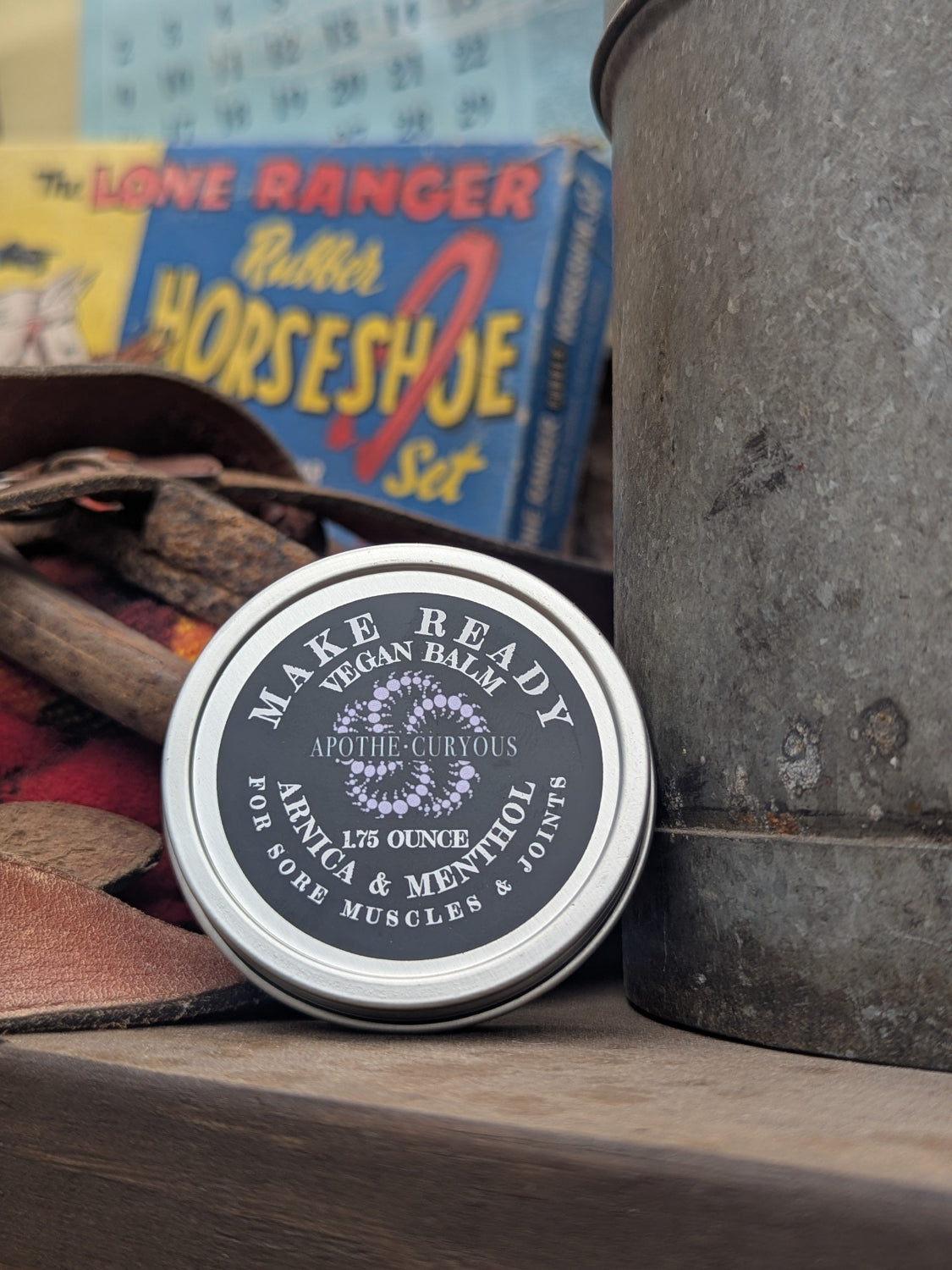 Vegan balm tin labeled 'Make Ready' on a wooden surface with vintage items in the background.