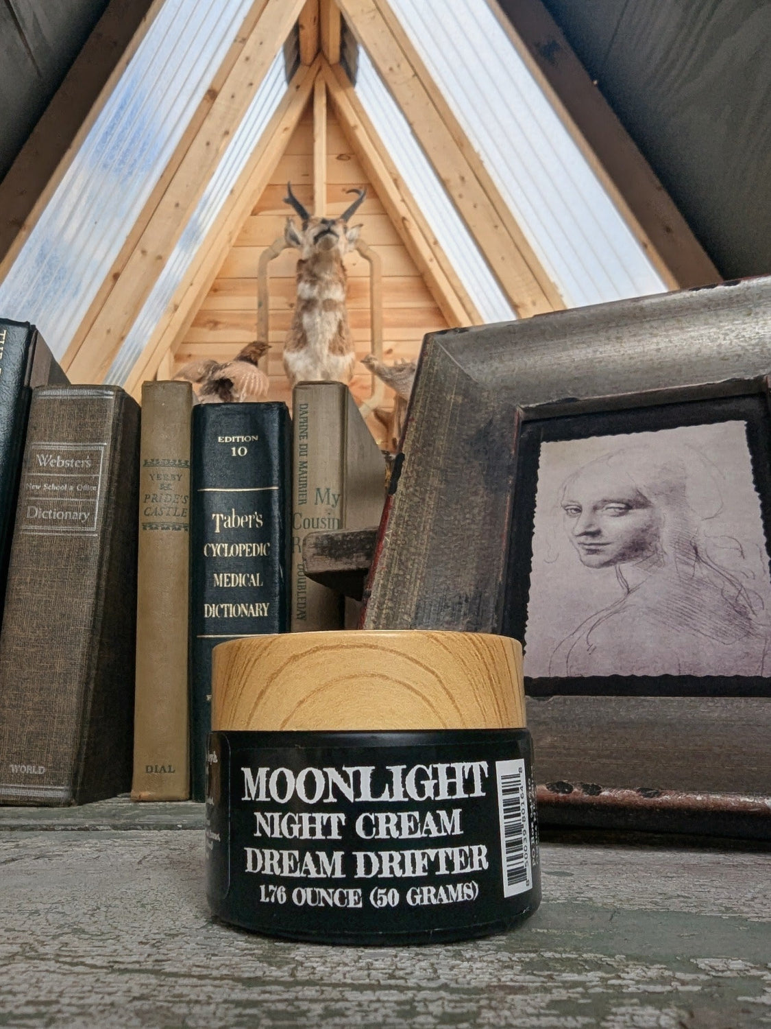Moonlight Night Cream container with a rustic background featuring books and a framed picture.