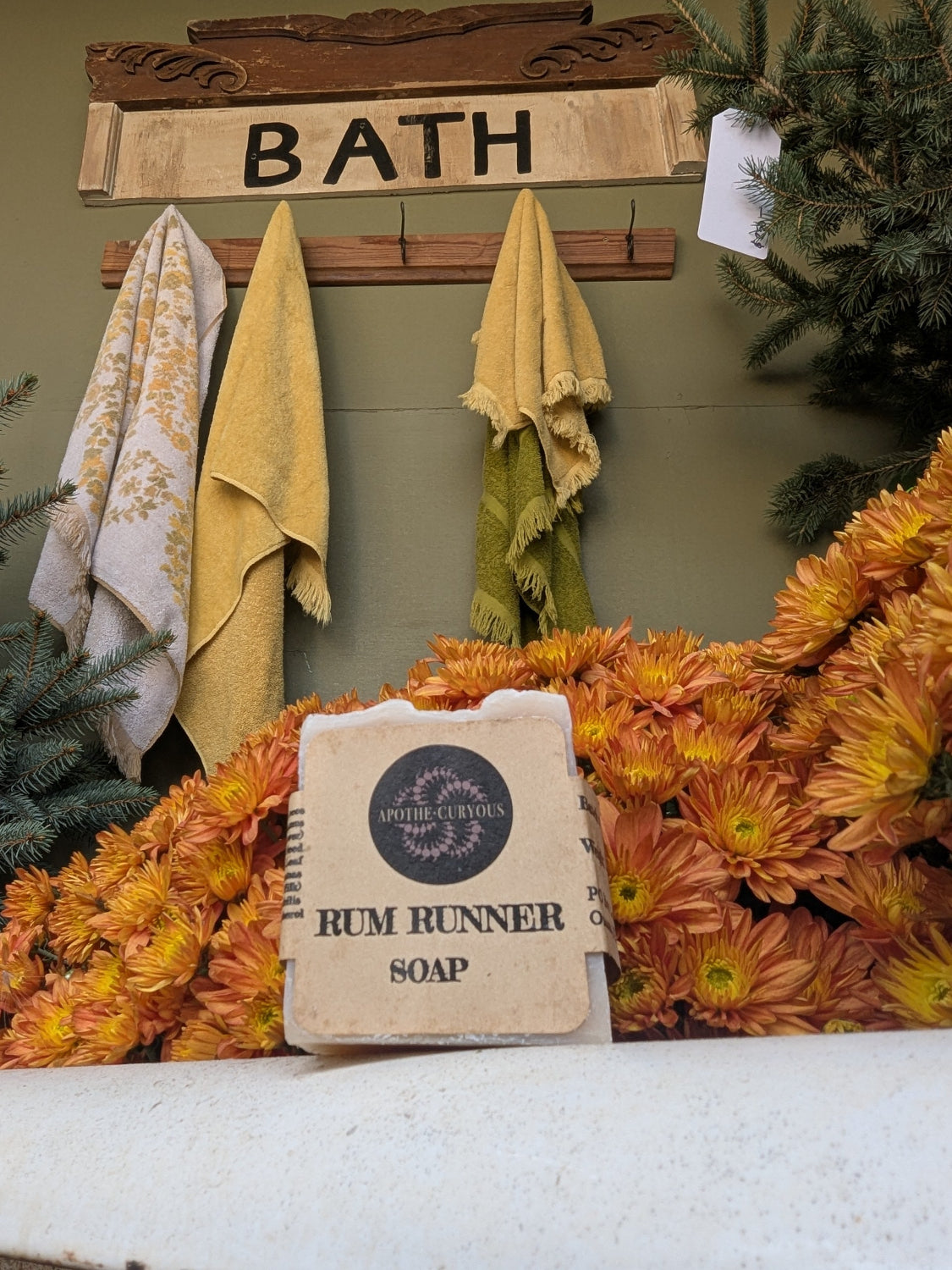Bar of soap with 'Rum Runner' branding on a surface with flowers and a 'Bath' sign in the background.
