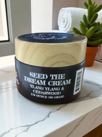 Jar of 'Seed the Dream Cream' with wooden lid on a marble surface.